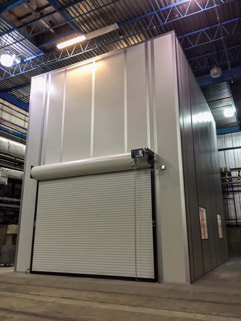 A large industrial roll-up door installed at the entrance of a warehouse with grey metal panels and a high ceiling lit by LED lights.